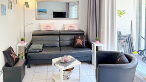 Un salón moderno con sofá, una mesa de centro y una silla. Hay un espejo grande sobre el sofá y una ventana con cortinas.
