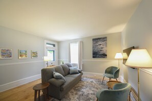A living room with a grey sofa, two armchairs, a small wooden side table, a patterned rug, and a painting on the wall. - Cozy Glebe Coach house perfect for smaller families (Ottawa)
