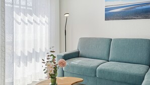 A living room with a light blue sofa, a wooden coffee table with a vase of flowers, and a floor lamp. - Modern "Ebbe&Flut" Vacation Rental in Norddeich for the Whole Family (Norddeich)