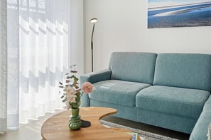 Ein Wohnzimmer mit einem hellblauen Sofa, einem Holztisch mit Blumen und einer Stehlampe.