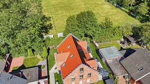 A residential area with a prominent red-roofed building, a green field, and a fenced sports field. - Modern "Ebbe&Flut" Vacation Rental in Norddeich for the Whole Family (Norddeich)