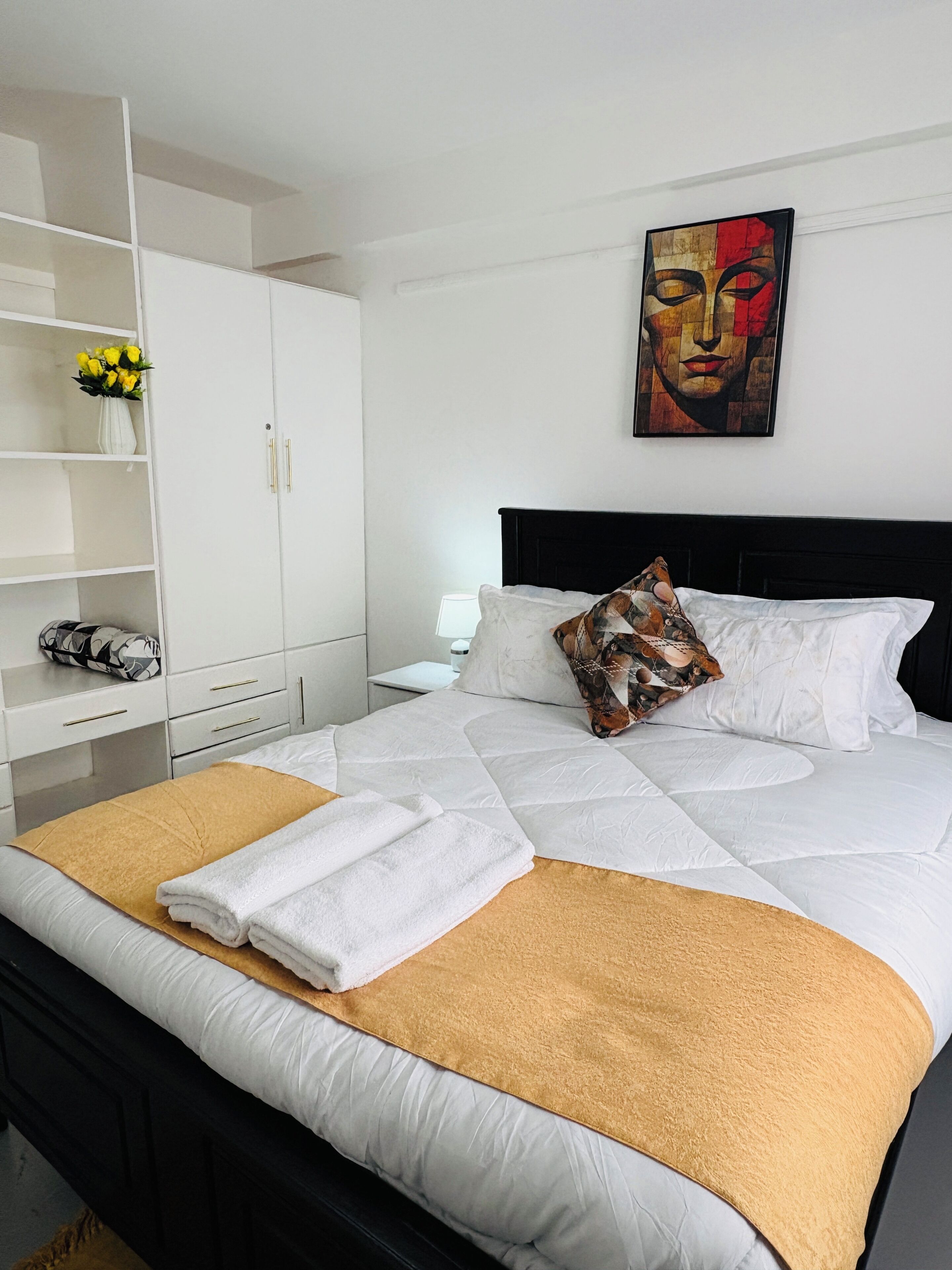 Una cama bien hecha con sábanas blancas, un plaid marrón y una almohada decorativa.