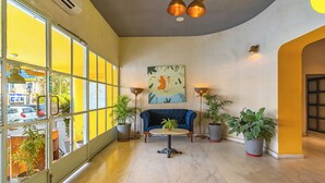 A spacious lobby with a blue sofa, potted plants, and a large window offering a view of the street.