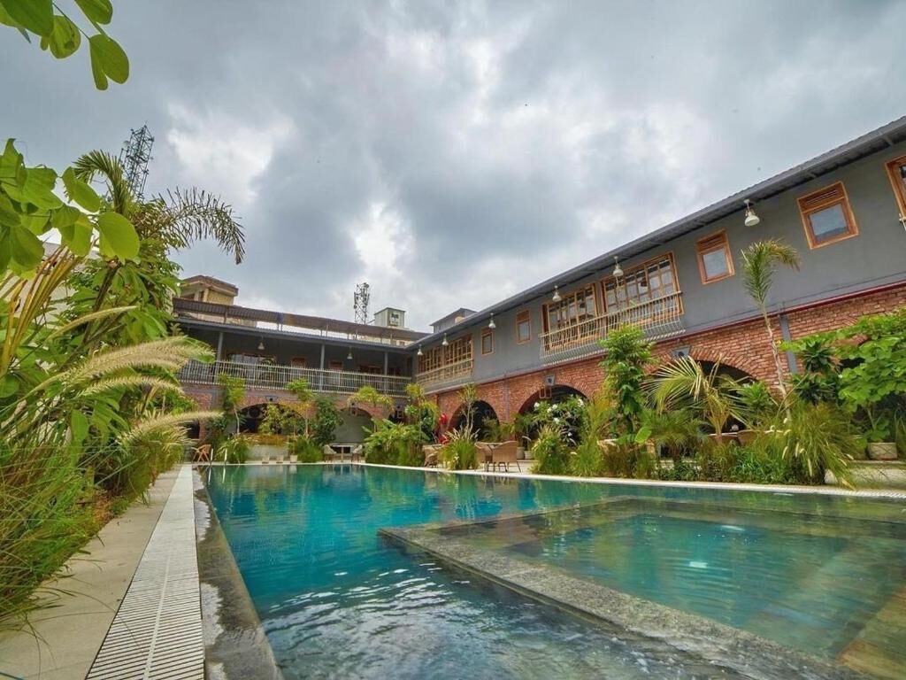 A swimming pool with a brick building in the background, surrounded by greenery.