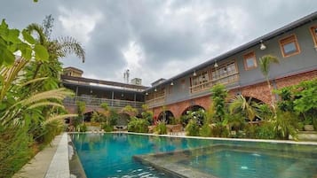 A swimming pool with a brick building in the background, surrounded by greenery.