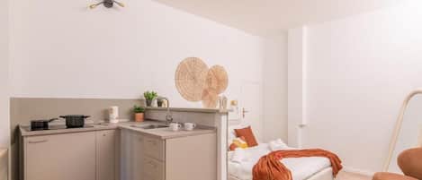 A compact room with a kitchenette, a bed with a brown blanket, and a chair.