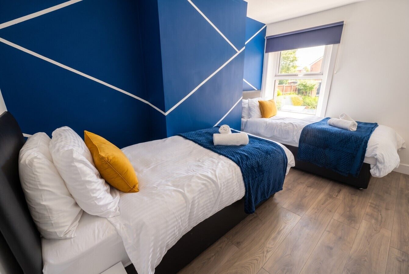 A hotel room with two beds, a blue accent wall, and a window with a view.