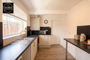A compact kitchen with a sink, microwave, toaster, and a clock on the wall. - 3-Bed House Sleeps 5 · Free Parking · Walk to Southampton Common (Shirley)