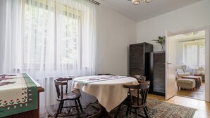 Uma área de refeições com uma mesa redonda, quatro cadeiras, um tapete estampado e uma janela com cortinas leves.