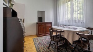 Ein Essbereich mit einem Tisch, Stühlen, einem Holzschrank und einem Fenster mit transparenten Vorhängen.