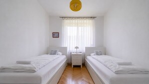 Ein Doppelzimmer mit zwei Betten, einem Nachttisch, einer Lampe und einem Fenster mit Vorhängen.