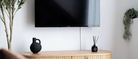 Ein modernes Wohnzimmer mit einem an der Wand montierten Flachbildfernseher, einem Holzschrank darunter, einer schwarzen Vase und einer kleinen Pflanze auf dem Schrank.