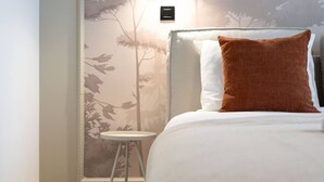 Una habitació d'hotel amb un llit, una tauleta de nit i una làmpada penjada a la paret.