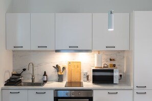Une cuisine moderne avec des armoires blanches, un évier en acier inoxydable, une planche à découper en bois, un grille-pain et un four à micro-ondes.