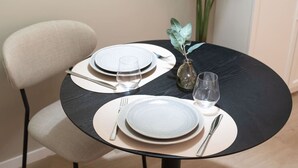 Ein Esszimmertisch mit Tellern, Besteck und Gläsern, dazu eine Vase mit einer Pflanze.