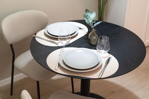 Ein Esszimmertisch mit Tellern, Besteck und Gläsern, dazu eine Vase mit einer Pflanze.
