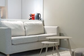 En moderne stue med en grå sofa, to runde sofaborde og en kaffemaskine på en hylde.