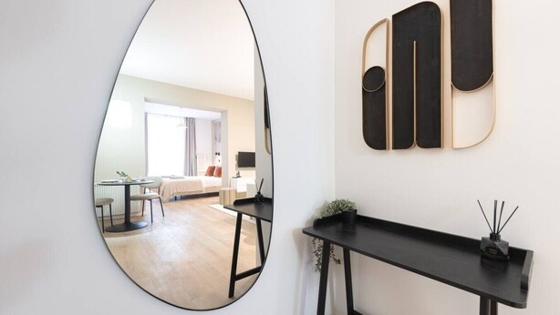 Ein modernes Interieur mit einem runden Spiegel, der einen Raum reflektiert, einem schwarzen Konsolentisch und einem an der Wand befestigten abstrakten Kunstwerk.