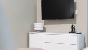Ein modernes Zimmer mit einem weißen Schrank, einem runden Tisch, einem an der Wand befestigten Fernseher und einer Skulptur.