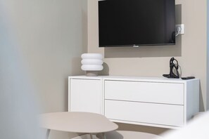 Ein modernes Zimmer mit einem weißen Schrank, einem runden Tisch, einem an der Wand befestigten Fernseher und einer Skulptur.