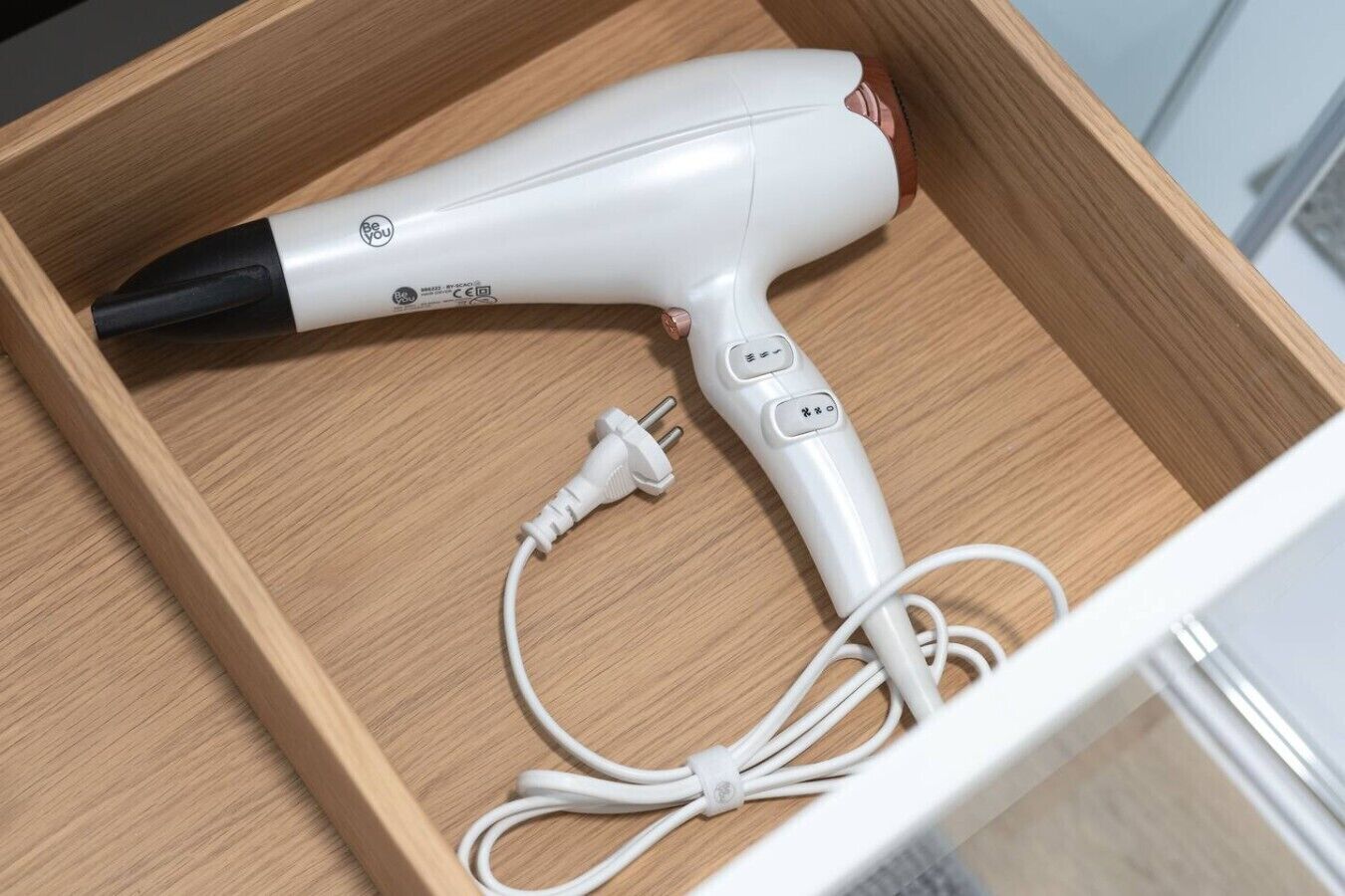 Ein weißer Haartrockner mit Kabel in einer Holzkiste.