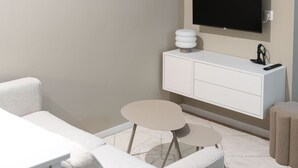 Ein modernes Hotelzimmer mit einem flachbildfernseher an der Wand, einer weißen Kommode mit Schubladen, einem kleinen runden Tisch und einem Sofa.