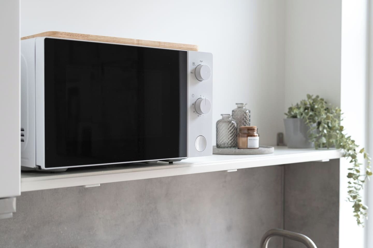 A microwave oven with a wooden top, placed on a white shelf.