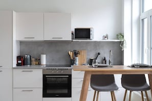 A modern kitchen with white cabinets, a built-in oven, a microwave, and a dining area with a wooden table and two chairs. - Modern Cocoon - Gare du Midi - BRO144.2.1 (Anderlecht)