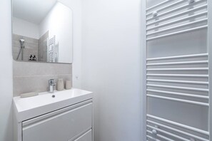 Een moderne badkamer met een wit wastafelmeubilair, een spiegel en een handdoekhouder.