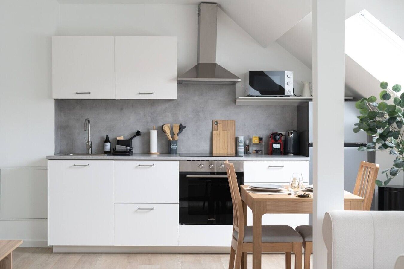 Een moderne keuken met witte kastjes, een magnetron, een fornuis en een eethoek met een tafel en stoelen.