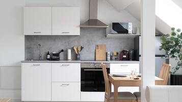 Een moderne keuken met witte kastjes, een magnetron, een fornuis en een eethoek met een tafel en stoelen.