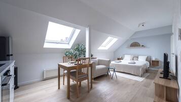 Een modern loft appartement met een eethoek, een zithoek en een slaapkamer. Er zijn dakramen voor natuurlijk licht, een flatscreen televisie en een inbouwkast.