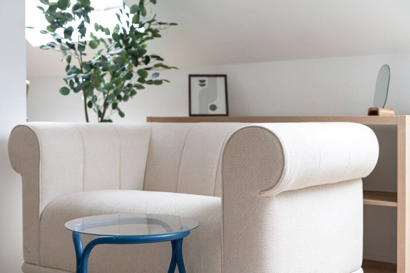 A modern living room with a beige sofa, a glass coffee table, and a wooden shelf.