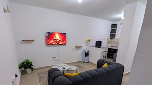 A living room with a black sofa, a TV displaying a fireplace, a small table, and a coffee machine. - Perfect apartment in Nairobi for a relaxing stay (Nairobi)