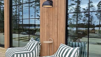 A wooden deck with two striped bean bag chairs and a small table, overlooking a body of water with trees.