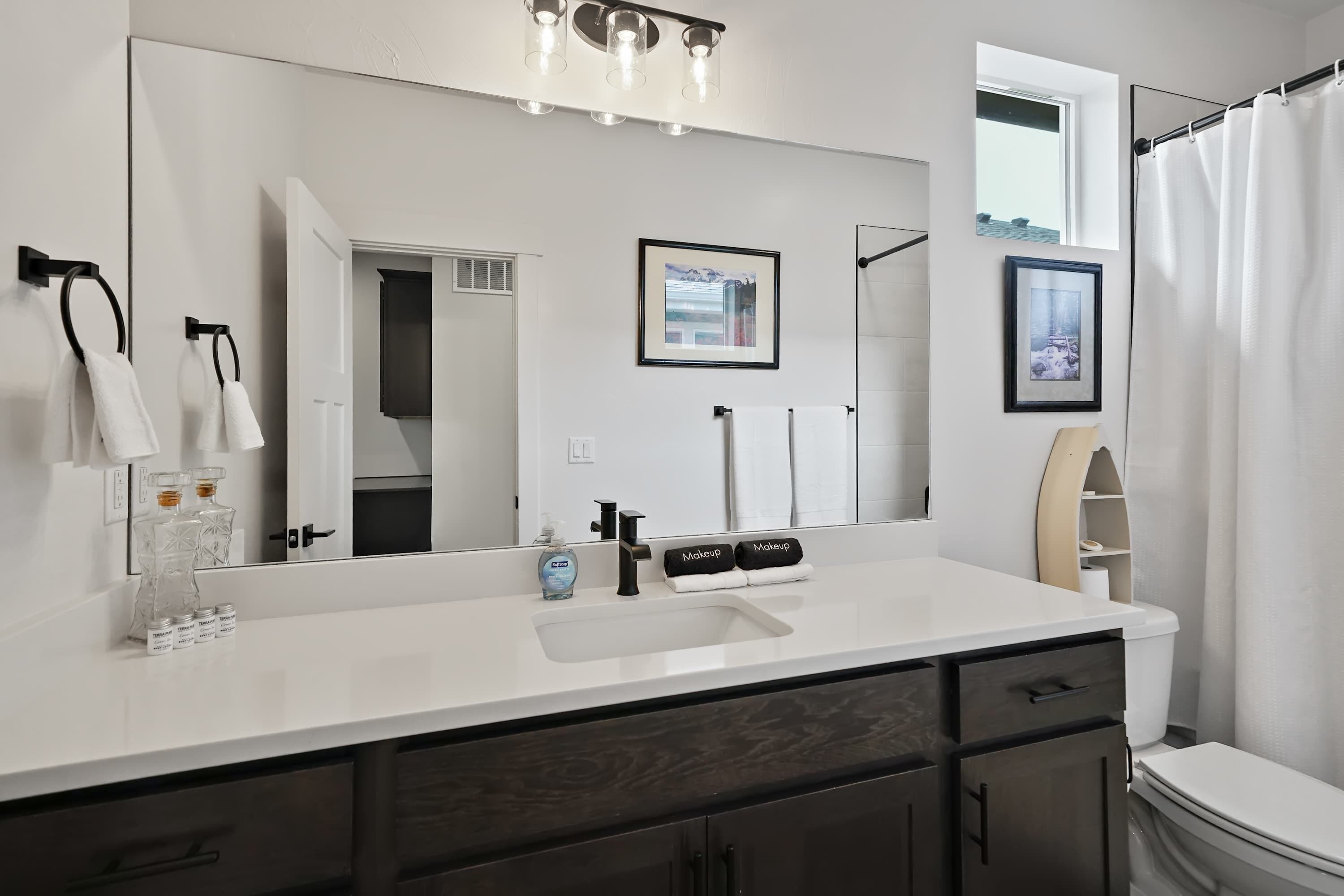 A modern bathroom with a large mirror, white countertop, dark wood cabinets, and a shower curtain.