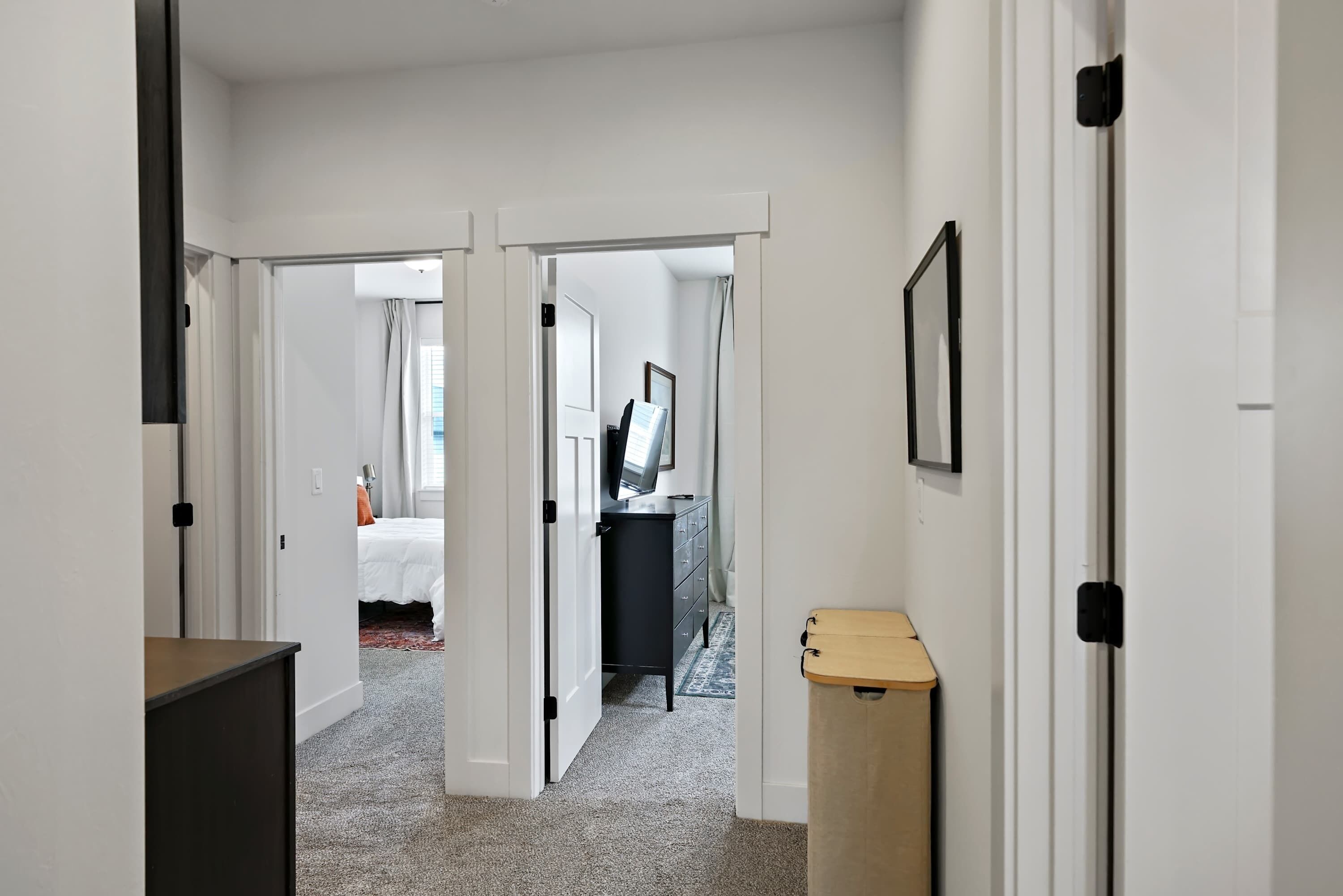 A hallway with a bed, a dresser, and a trash bin.