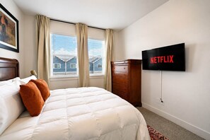 Et hotelværelse med en seng, en kommode, et fjernsyn ophængt på væggen og et vindue med gardiner.