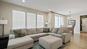 A modern living room with a sectional sofa, a dining area, and a chandelier.