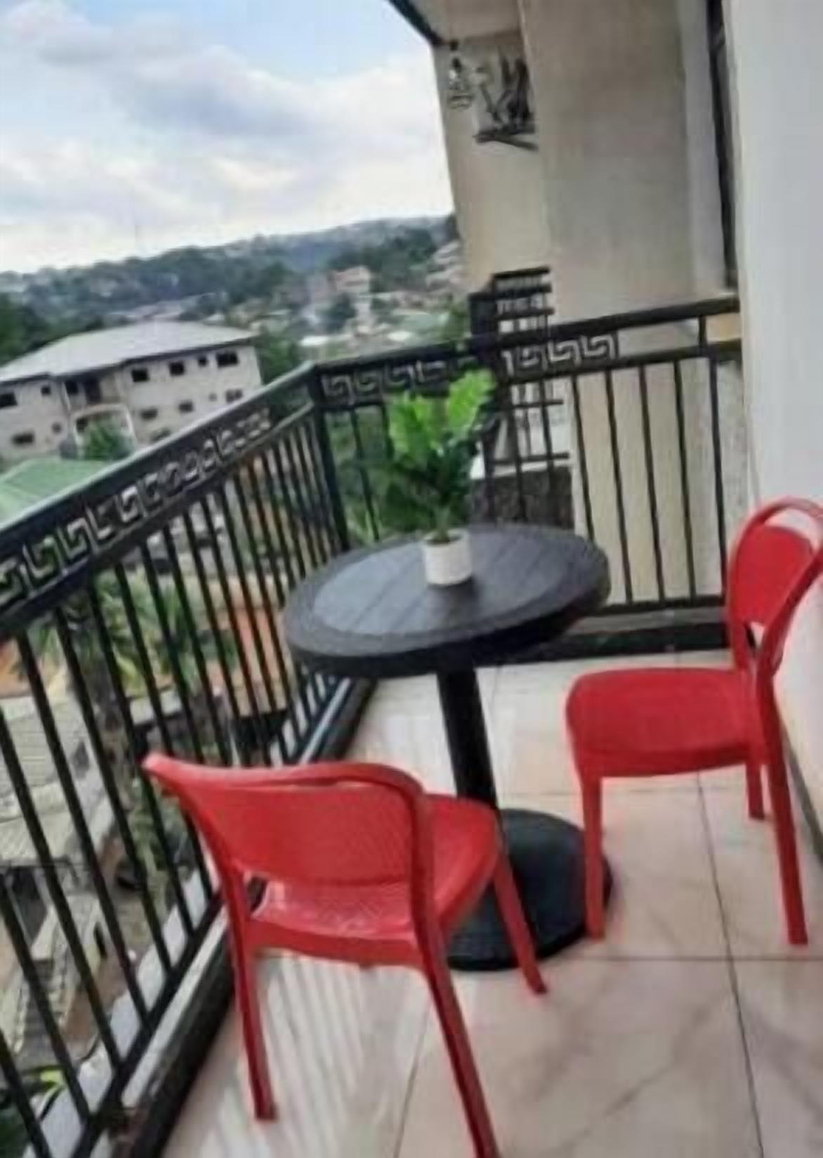 Un balcon avec une table ronde et deux chaises, une balustrade et une vue sur des bâtiments situés au loin.