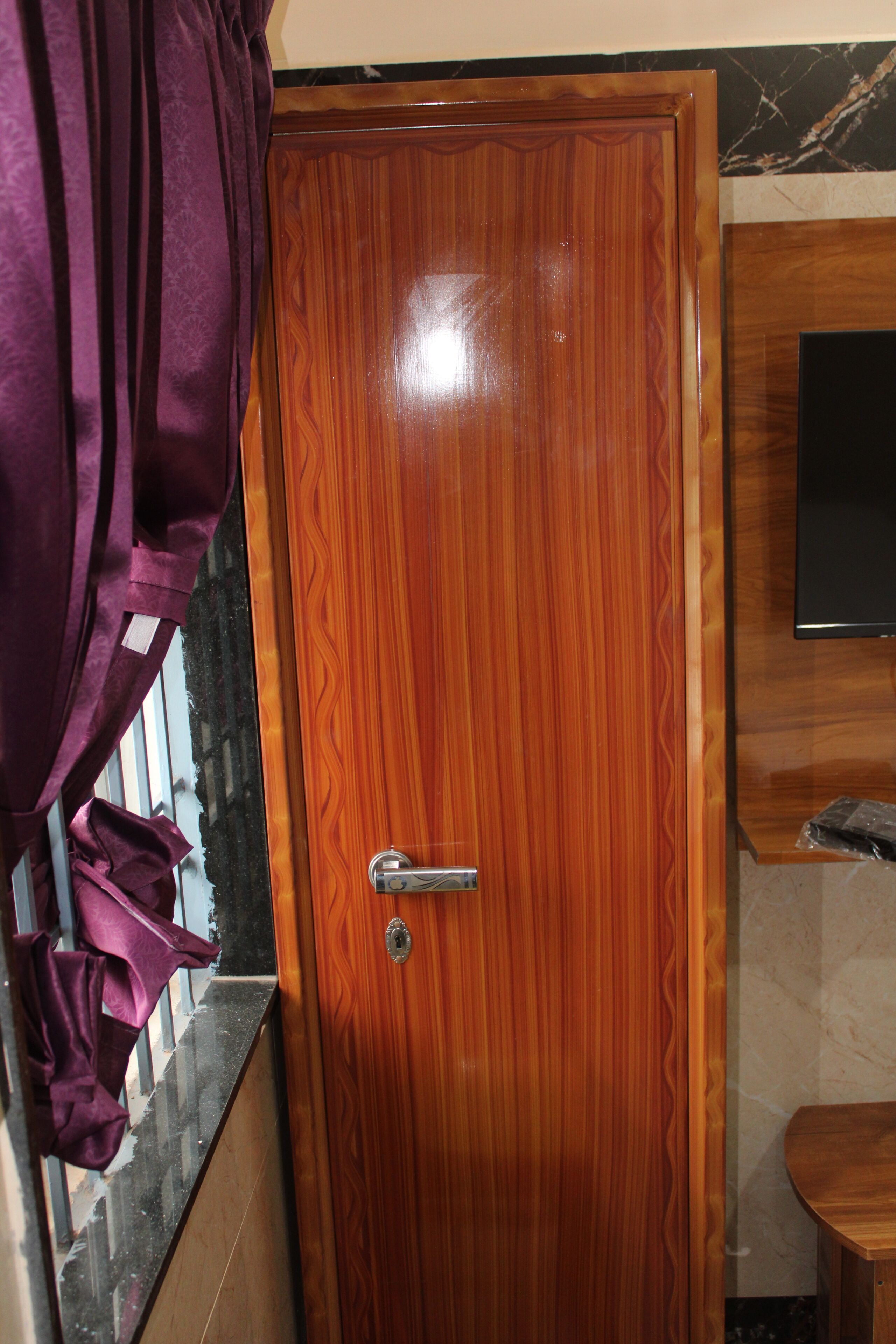 A wooden door with a metal handle and a keyhole, a purple curtain partially covering a window, and a marble countertop.