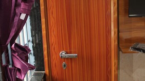 A wooden door with a metal handle and a keyhole, a purple curtain partially covering a window, and a marble countertop. - Srivari Lodge (Aarkadu)