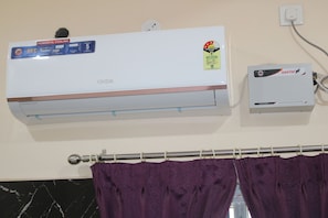 A wall-mounted air conditioner with a power savings guide sticker, a wall socket, and a curtain rod with purple curtains.