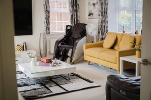 Ein Wohnzimmer mit einer Couch, einem Massagesessel, einem Couchtisch und einem Ventilator.