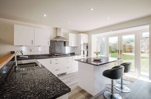 A modern kitchen with granite countertops, stainless steel appliances, and a central island with bar stools. - Spacious 5-bed Home in Milton Keynes by Renzo, Driveway Parking, Close to M1 (Milton Keynes)