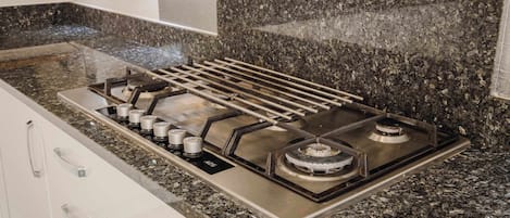 Una cocina con estufa a gas, encimera de granito y muebles de cocina blancos.