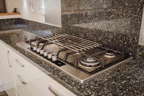 A kitchen with a gas stove, granite countertop, and white cabinetry. - Spacious 5-bed Home in Milton Keynes by Renzo, Driveway Parking, Close to M1 (Milton Keynes)