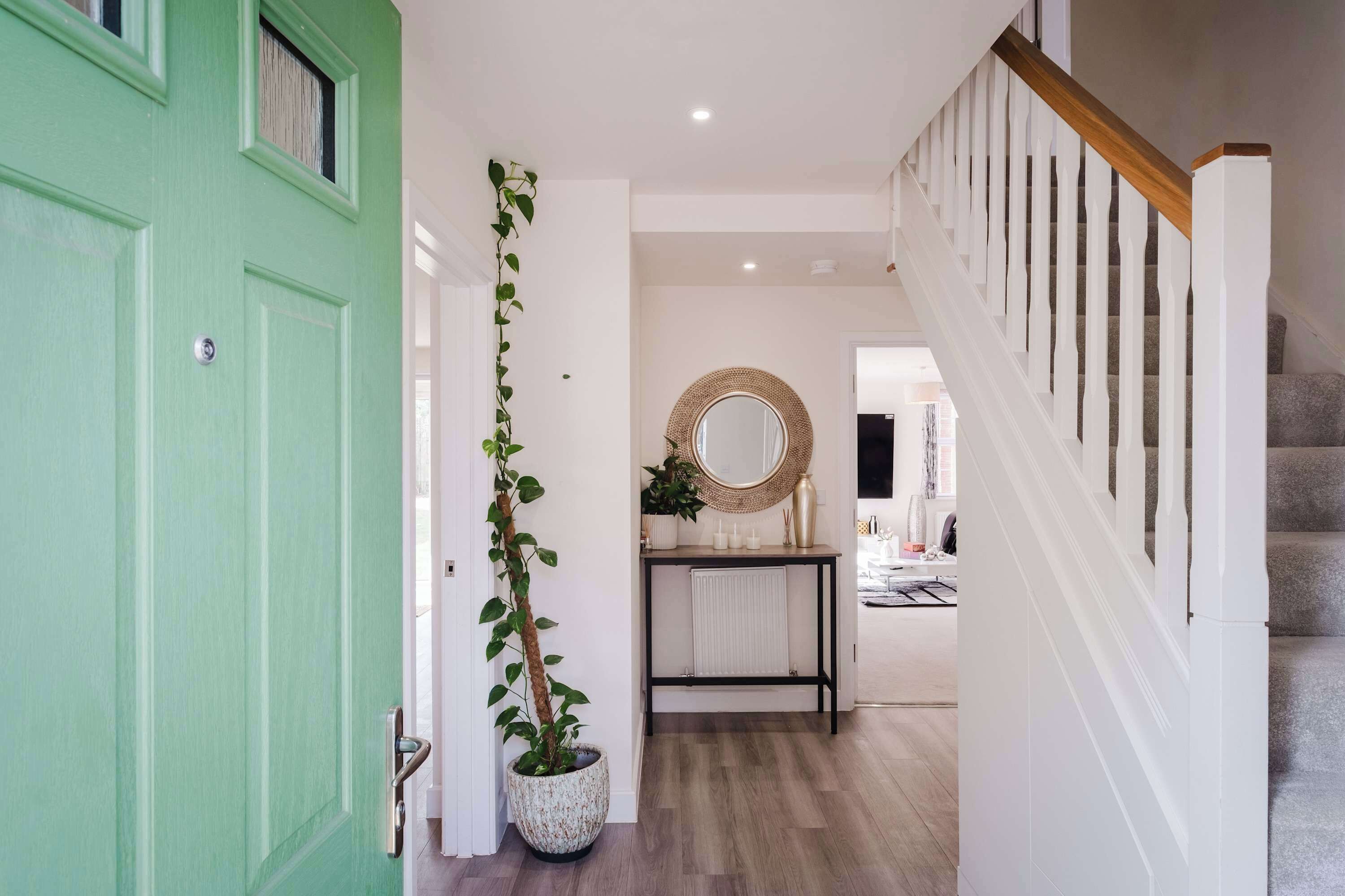 A hallway with a green door, a potted plant, a mirror, and a staircase.