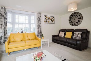 Ein Wohnzimmer mit einem gelben Sofa, einem schwarzen Ledersofa, einem weißen Couchtisch und einer großen Wanduhr.