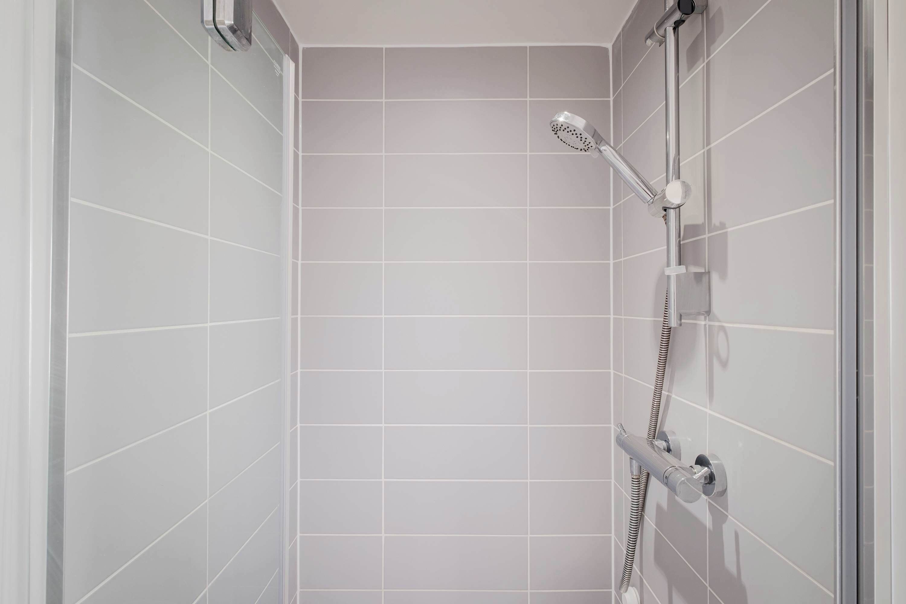 Une douche équipée d’un pommeau de douche à main et d’un robinet fixé au mur.